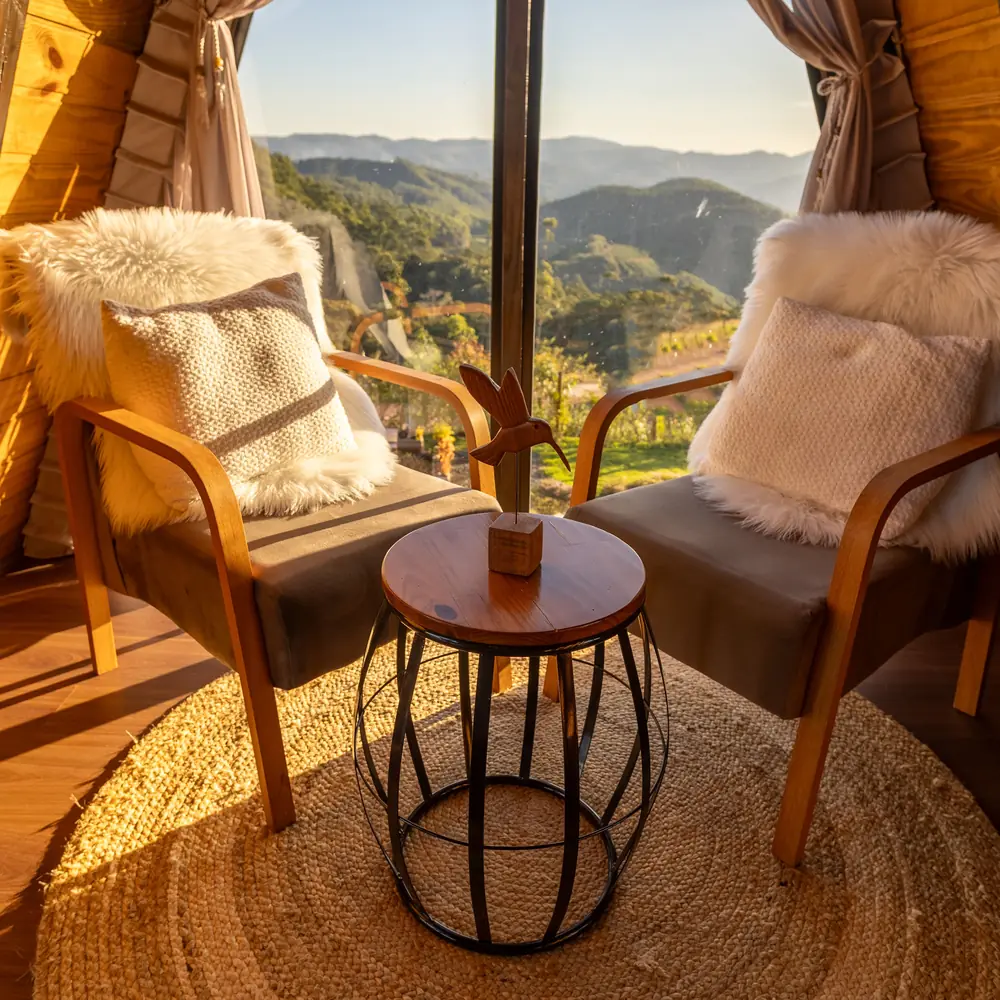 Two armchairs with sheepskins and a small round table in the sunlit glass end of an A-frame cabin