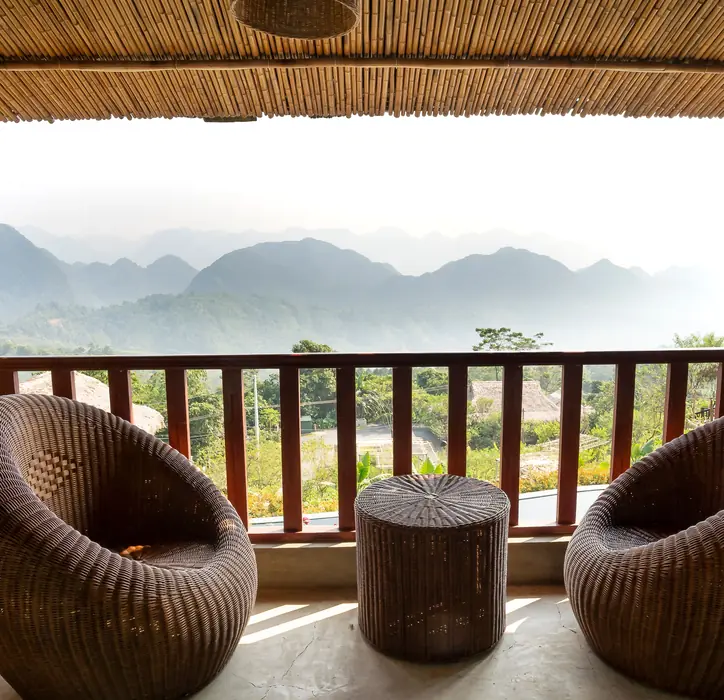 Two round wicker armchairs on a covered balcony, looking over misty mountains