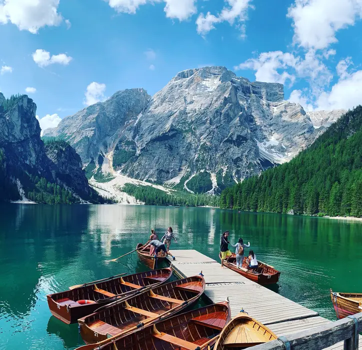 Wooden rowing boats tied along a jetty on a green mountain lake, grey peaks above